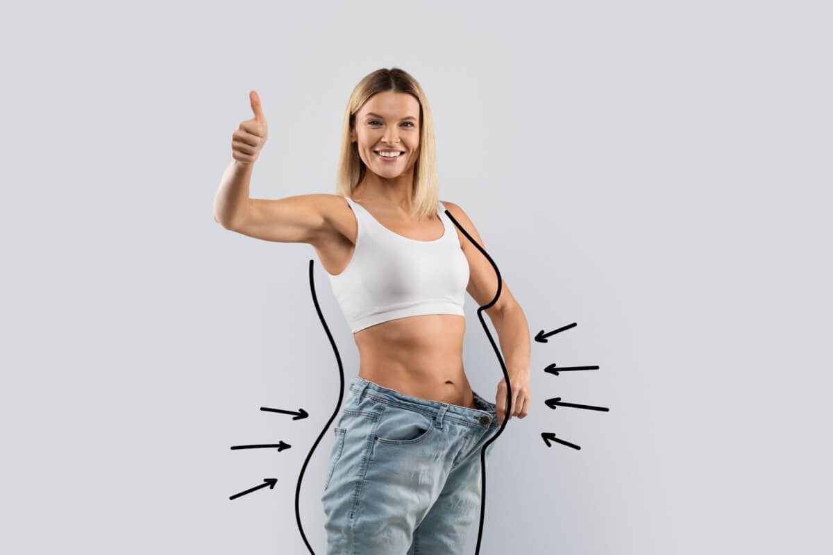 Mulher sorridente mostrando a cintura menor em uma calça larga, representando o emagrecimento sustentável