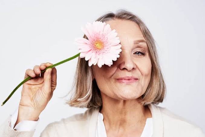 Mulher madura sorrindo com uma flor sobre um dos olhos, representando a saúde da mulher 40+ e a menopausa